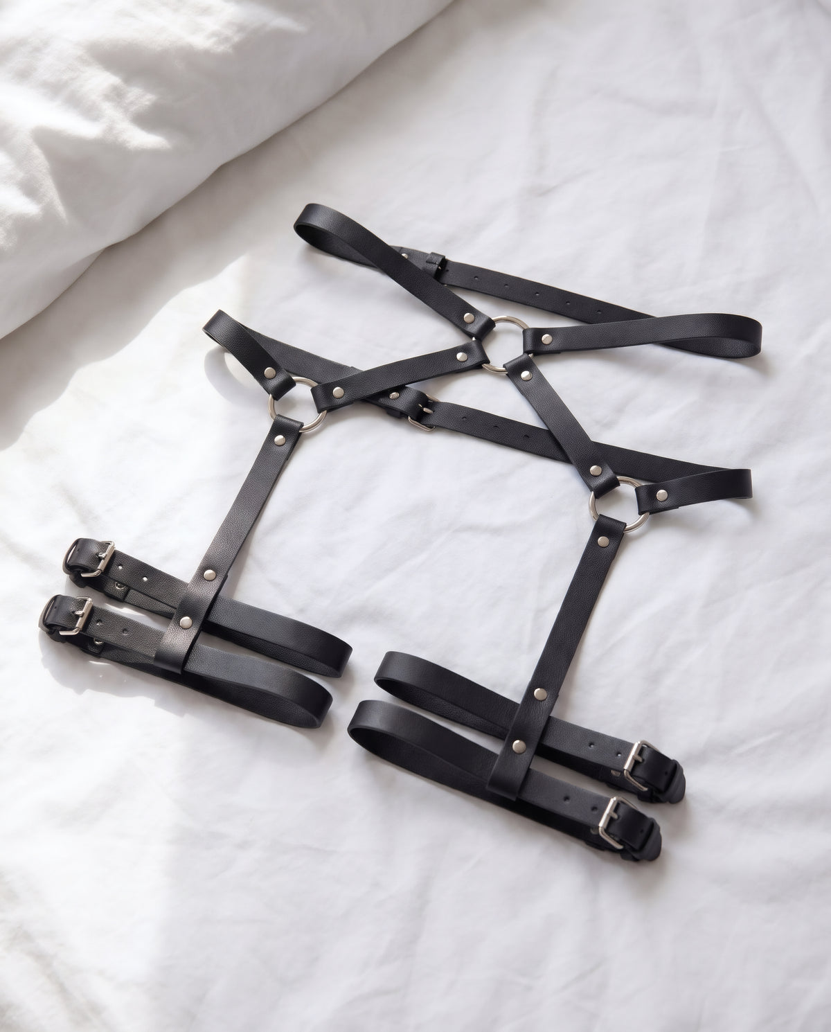 Harnais Lou en cuir vegan noir posé sur un drap blanc froissé