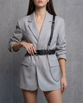 Harnais Styx en cuir vegan noir porté sur un blazer gris perle, vue de face : ceinture, bretelle d'épaule et chaîne