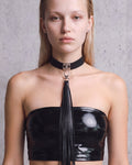 Collier ras-de-cou Zelda en cuir vegan noir à plaque argentée et long pompon de franges, porté de face avec un bandeau en vinyle noir