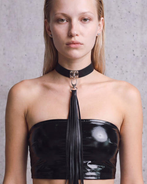 Collier ras-de-cou Zelda en cuir vegan noir à plaque argentée et long pompon de franges, porté de face avec un bandeau en vinyle noir